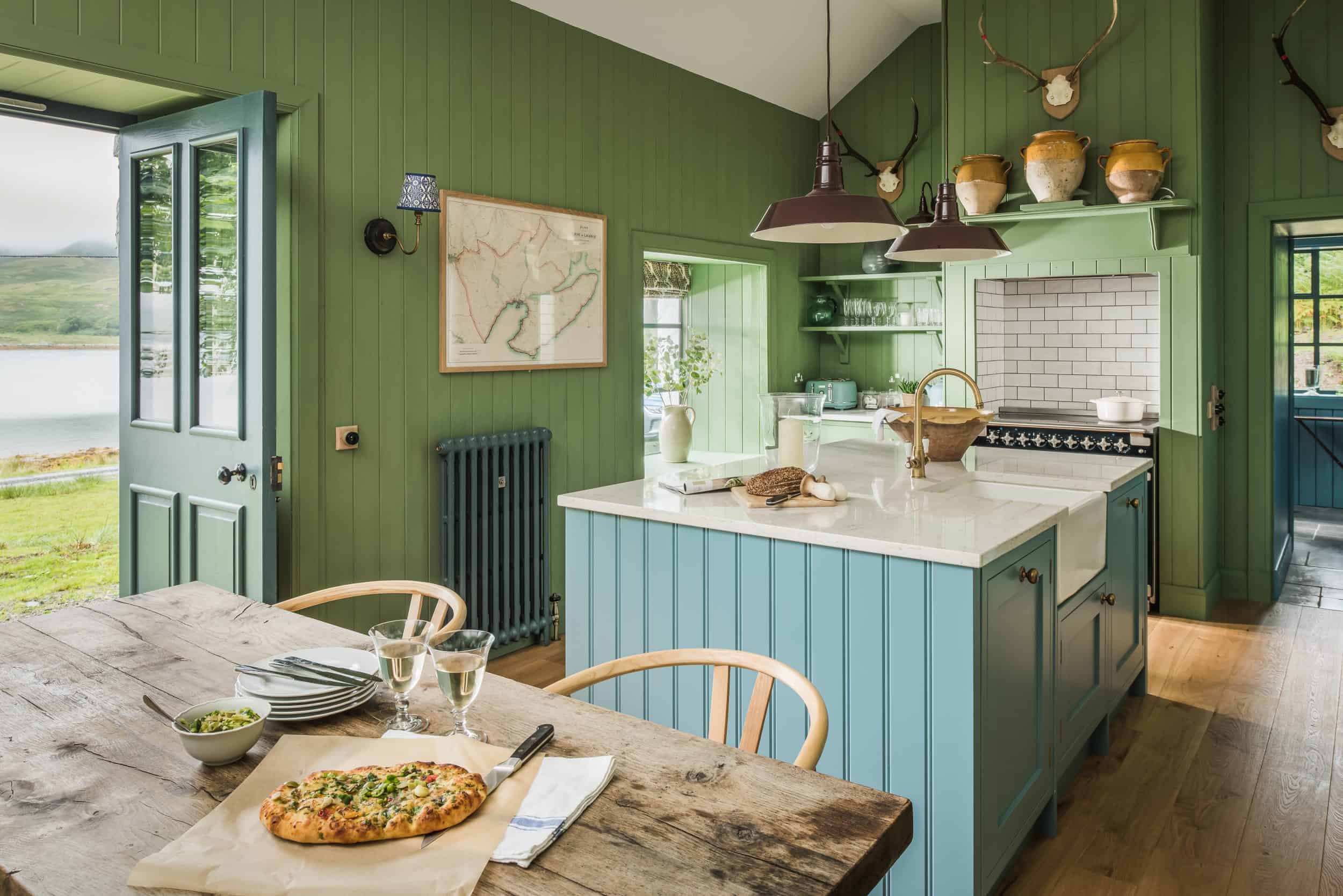 John Lewis of Hungerford luxury shaker style cottage kitchen with bright green wooden panel walls and turquoise blue kitchen island with white worktop and a rustic wooden dining table